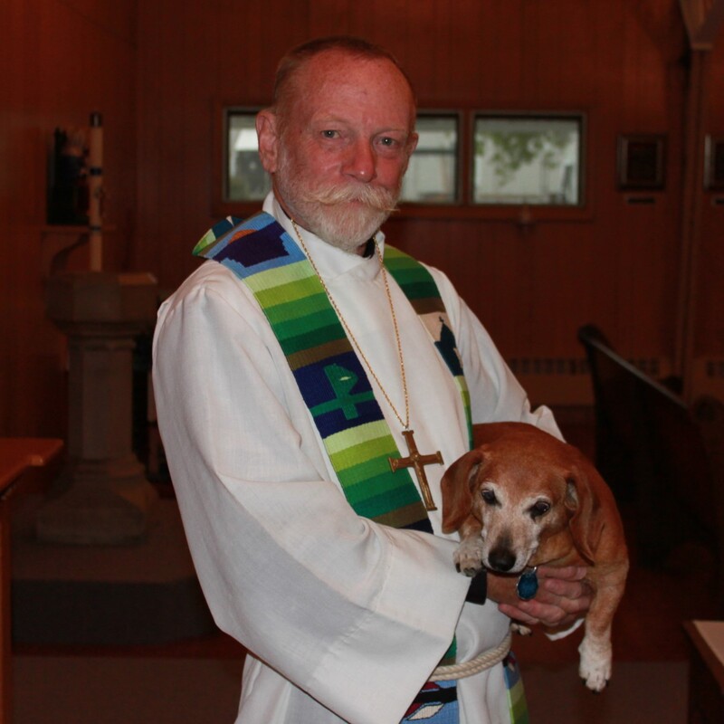 male priest in robe and stole, holding dachshund